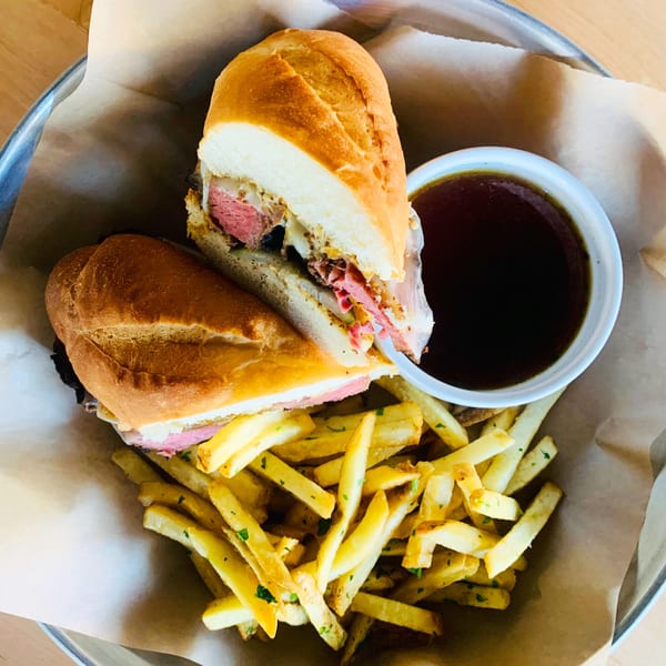 A French dip sandwich with fries and a side of au jus in a metal basket.