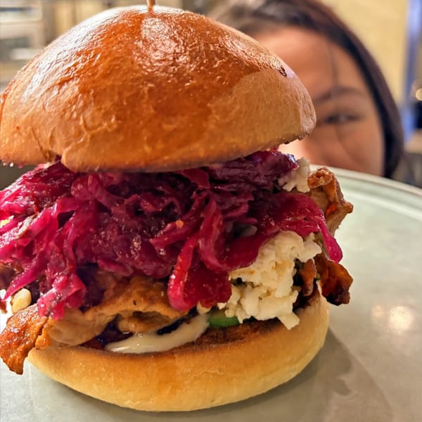 A burger with bright red pickled onions, white cheese, and meat, with a person in the background.
