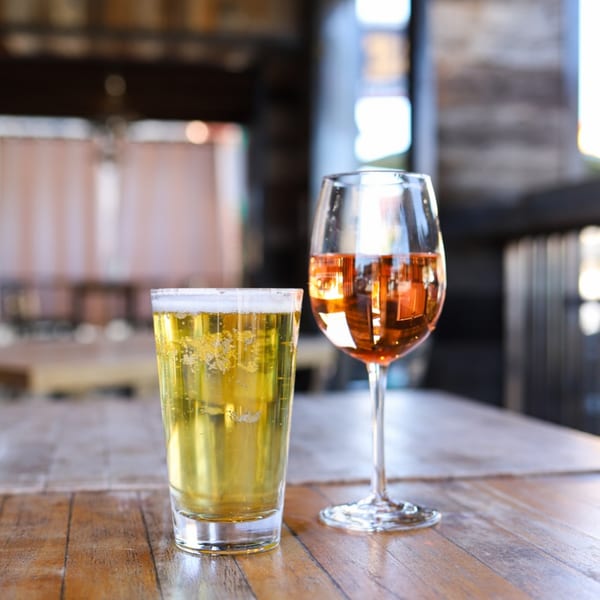 A glass of golden beer and a stemmed glass of amber wine on a wooden table at 38 Degrees Ale House & Grill.