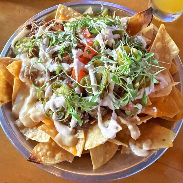 A large plate of nachos with melted cheese, meat, jalapeños, tomatoes, and microgreens.