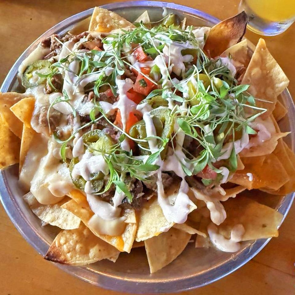 A large plate of nachos with melted cheese, meat, jalapeños, tomatoes, and microgreens.