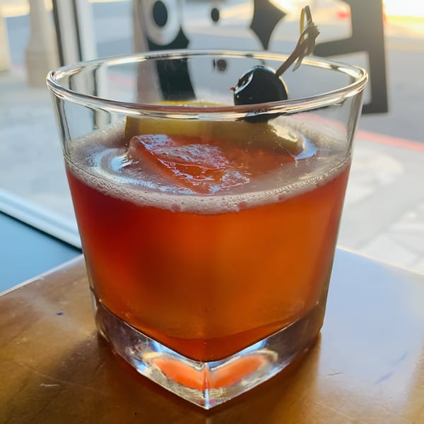 A vibrant orange cocktail with a large ice cube, lemon slice, and cherry garnish in a glass.