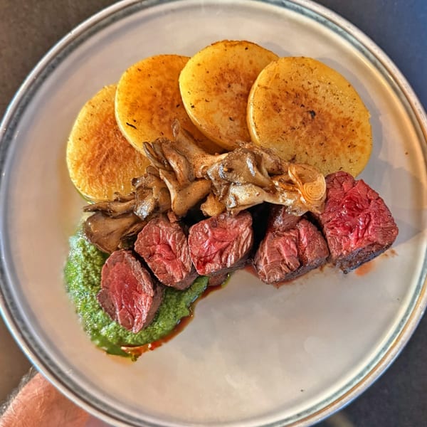 Sliced steak with green sauce, roasted potatoes, and mushrooms on a white plate.